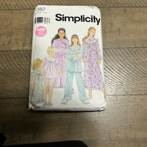 May include: A Simplicity sewing pattern packet with illustrations of sleepwear designs. The packet is white with the brand name in bold black letters. The designs include a robe, pyjamas, and nightgowns. The size range is K5 7-14.