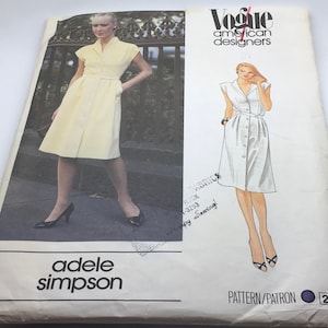 Peut inclure: Un patron de couture vintage Vogue American Designers, design Adele Simpson. La couverture présente une robe jaune avec un devant boutonné, des manches courtes et une ceinture. Le texte "adele simpson" est visible.