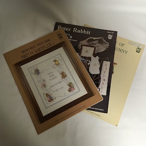 Op de afbeelding: Drie kruissteekpatronen met Beatrix Potter-personages. Het eerste patroon is een geboorte-sampler met de tekst "James Bryant June 16, 1922 June 11th, '22 The ..." Het tweede patroon is een Peter Rabbit-ontwerp met een baby in een kinderwagen. Het derde patroon is een konijnenontwerp met de tekst "The ... of Bunny".
