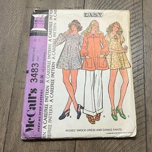 May include: Vintage McCall's 3483 sewing pattern for Misses' smock dress and dance pants. The pattern features illustrations of three different outfits. The cover is purple and white with the word "EASY" in a white box.