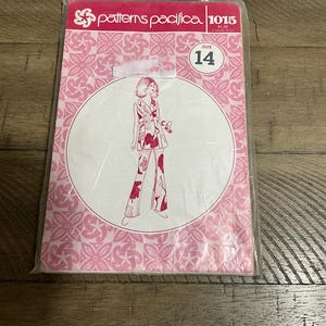 Op de afbeelding: Een Patterns Pacifica naaipatroon envelop, nummer 1015, maat 14. De verpakking is roze en wit met een herhalend bloemenpatroon. Het heeft een centrale witte cirkel met een lijntekening van een jasje en een broek met wijde pijpen.