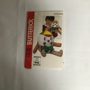 May include: A vintage sewing pattern for a clown doll. The pattern is from Butterick and is number 237. The pattern is for a craft project and costs $3.65. The pattern shows a red and white checkered doll with a yellow hat and a green collar.