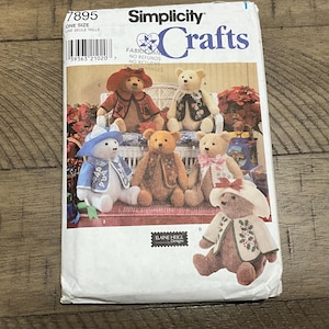 Op de afbeelding: Simplicity Crafts naaipatroon met teddyberen in verschillende outfits. Het patroon bevat instructies voor het maken van verschillende pluche beren met verschillende kleding en accessoires. De verpakking is wit met het nummer 7895 en de woorden "ONE SIZE" erop gedrukt.