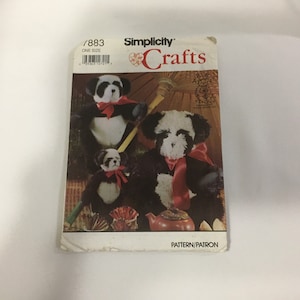 May include: Simplicity Crafts pattern number 7883, one size, for making panda bears. The pattern shows three panda bears, one large, one medium, and one small, all with black and white fur and red ribbon accents. The pattern also includes a teapot and a parasol.