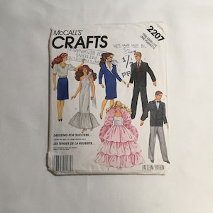 May include: McCall's Crafts sewing pattern number 2207 for dressing dolls. The pattern includes a blue blazer, a white dress with a ruffled hem, a pink gown with a ruffled skirt, a black suit, and a black tuxedo. The pattern is titled "Dressing for Success..." and "Les Tenues de la Reussite..."