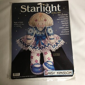 May include: A doll kit featuring a blue and white dress with a pink heart design. The doll is 18 inches tall and comes with instructions for making the doll and her clothes. The kit is called "Starlight" and is from Daisy Kingdom.