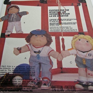Könnte beinhalten: Ein Schnittmuster zum Nähen von Kleidung für Cabbage Patch Kids Puppen. Das Schnittmuster enthält drei verschiedene Outfits: ein gestreiftes Hemd und eine Hose, ein rot-weiß gestreiftes Hemd und eine Hose sowie ein blau-weiß gestreiftes Hemd und eine Shorts. Das Schnittmuster ist für Puppen geeignet, die 30,5 cm, 40,5 cm oder 46 cm groß sind. Das Schnittmuster heißt "Kleidung für das sportliche Leben".