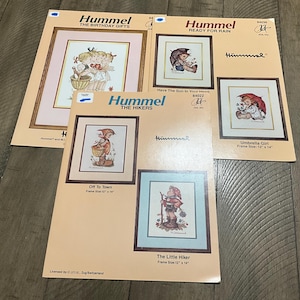 May include: Several Hummel framed art prints are displayed, featuring children in various scenes. The prints include titles like "The Birthday Gifts," "Ready for Rain," and "The Hikers." Frame sizes are 12" x 14" and 13" x 16". The prints have a light peach background.
