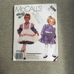 May include: McCall's sewing pattern number 3398 for girls' dresses in sizes 4, 5, and 6. The pattern includes two dress designs: a white and pink gingham dress with a ruffled apron and a purple polka dot dress with a white sash.