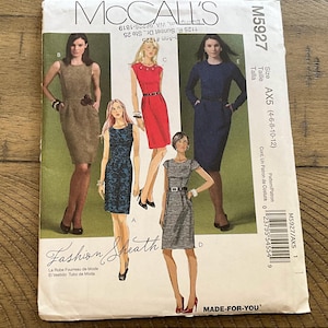 May include: McCall's sewing pattern M5927 for a fashion sheath dress. The pattern features illustrations of various dress styles, including a red dress with a belt and a navy blue long-sleeved dress. The pattern size is AX5 (4-6-8-10-12).