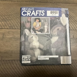 May include: A vintage McCall's Crafts sewing pattern for making two huggable, stuffed bunnies. The pattern is number 8951 and costs $5.70. The pattern features a photo of a child holding a completed bunny and a close-up of the bunny's head.
