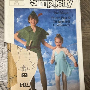 May include: A Simplicity sewing pattern envelope 7784 for Walt Disney's Peter Pan and Tinkerbell costumes. The front shows a child in a green tunic and hat, and another child in a light blue dress with wings. The paper envelope is torn at the bottom.