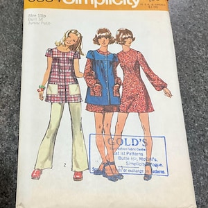 May include: A Simplicity 9834 sewing pattern envelope for size 11jp, bust 34, featuring illustrations of three outfits: a plaid tunic with pants, a blue button-front dress with long sleeves, and a red floral print long-sleeve dress with a blue stamp.