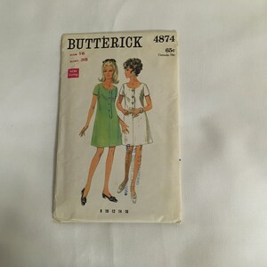 Op de afbeelding: Vintage naaipatroon voor een jurk, Butterick 4874, maat 16, borstomvang 38. Het patroon toont twee vrouwen die een groene en een witte jurk dragen. Het patroon kost 65 cent.