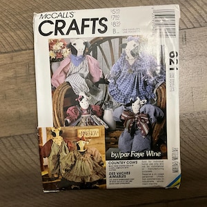Op de afbeelding: Een vintage McCall's Crafts naaipatroon voor het maken van country cow poppen. Het patroon is voor 621 en bevat instructies voor het maken van twee knuffelpoppen met kleding. De patroonhoes heeft een kleurrijke illustratie van vier koepoppen.