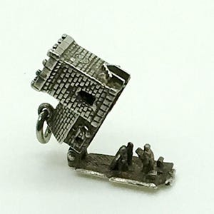 Puede incluir: Encanto de plata en forma de castillo con una puerta con bisagras que se abre para revelar una escena de personas en el interior. El encanto es detallado e intrincado.