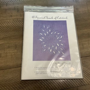 May include: A purple paper craft project with a flower design. The title "A Special Touch of Cutwork" is at the top of the page. The text "by Kainy Chorashi" is at the bottom of the page. The instructions include step-by-step instructions for two projects, simplified and fully illustrated. The instructions also include a sample project, additional techniques, a pattern, and extra cutwork designs.