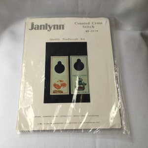 May include: A Janlynn counted cross stitch kit with a rooster and a stove design. The kit includes evenweave fabric, cotton floss, a needle, a graph, and instructions. The kit number is 37-4026.