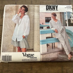 May include: A DKNY Vogue Patterns sewing pattern envelope, number 2703, featuring two garment variations: a white long-sleeve button-down shirt with a light gray skirt, and a light gray long-sleeve button-down shirt with matching light gray trousers.