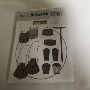 May include: A sewing pattern for a historical costume, featuring a variety of accessories, including a belt, pouches, and arm guards. The pattern is labeled "B5371 Butterick" and "HISTORY".