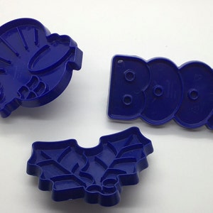 Könnte beinhalten: Drei blaue Plastik-Ausstecher, einer in Form eines Truthahns, einer in Form eines Stechpalmenblattes und einer in Form des Wortes "BOO".