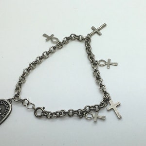 May include: Silver chain bracelet with a silver oval charm that says "Graduation 2005" and has a cross on it. The bracelet also has several silver cross and ankh charms.