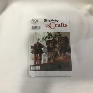 Könnte beinhalten: Ein Simplicity Crafts-Schnittmusterumschlag mit drei Teddybär-Puppen. Die Bären sind in verschiedenen Outfits und mit Accessoires gekleidet. Der Umschlag trägt die Nummer 7000 und die Aufschrift "Simplicity Crafts".