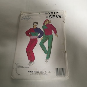 May include: A sewing pattern for a two-piece outfit, featuring a hooded sweatshirt and matching pants. The pattern is designed by Kwik Sew and features a woman wearing the outfit in a variety of poses. The pattern is for sizes A and B.