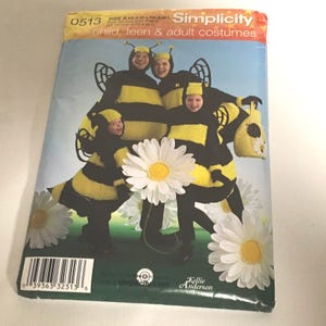 May include: A Simplicity sewing pattern envelope 0513 for child, teen, and adult bee costumes. The cover features four individuals wearing black and yellow striped bee outfits with antennae headpieces and wings, surrounded by large white daisy flowers.