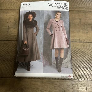May include: A Vogue Patterns V1971 sewing pattern envelope featuring two coat designs. One is a long, brown, double-breasted coat with a dark faux fur collar. The other is a shorter, light pink, double-breasted coat with a wide collar and flared skirt.