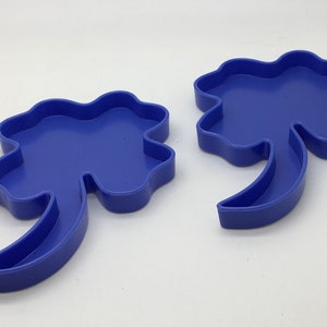 May include: Two blue plastic four-leaf clover cookie cutters with a stem.