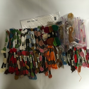May include: A large collection of embroidery floss in various colors, organized in bundles and labeled with numbers. The floss is packaged in clear plastic bags and includes a project card labeled "DMC Project Card".