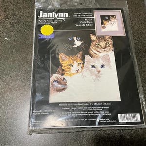 May include: A counted cross stitch pattern featuring a close-up of five cats with different coloured fur. The pattern is titled "Cat's Eyes" and is from Janlynn, a family business established in 1979. The finished size is 9 inches by 12 inches.