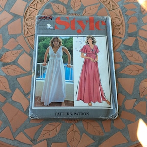 May include: A vintage sewing pattern for a maxi dress with a V-neckline and a tie at the waist. The pattern is for sizes small to medium and is labeled "Style".
