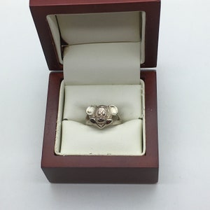May include: A silver ring featuring a Mickey Mouse head design, presented in a brown ring box.