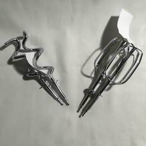May include: Two silver metal attachments for a stand mixer. One attachment is a spiral shaped dough hook and the other is a flat beater.
