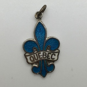 May include: A silver charm with a blue enamel fleur-de-lis and a white enamel banner that reads "QUEBEC".