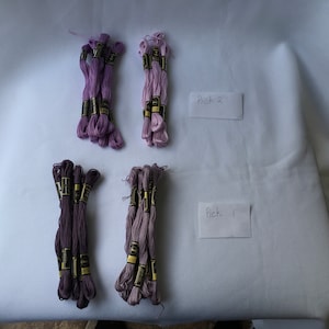 May include: Four bundles of embroidery floss in various shades of purple and lavender. The bundles are arranged in two rows of two. The top row is labeled "Pick 2" and the bottom row is labeled "Pick 1".
