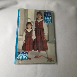 May include: A sewing pattern for a plaid dress for girls. The pattern is for sizes 7-8-10 and is from the see & sew brand. The pattern is called "Now" and the number is 6332. The pattern is for a dress with a white collar and buttons down the front.