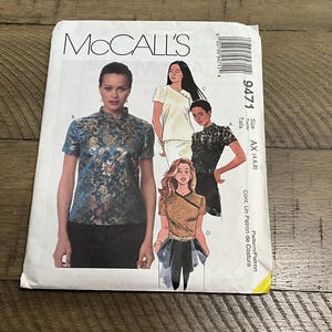 May include: A McCall's 9471 sewing pattern envelope featuring illustrations of four different top designs. The front shows a blue floral print mandarin collar top, a cream crossover top, a black lace top, and a tan top with a dark trim and sash.