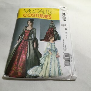 May include: A McCall's Costumes sewing pattern for a gown, featuring a model wearing a burgundy and green gown with a lace trim. The pattern number is M6097 and the size is AA (6-8-10-12).