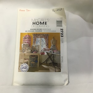 May include: McCall's Home Decorating sewing pattern envelope, featuring a sewing room with a table, chair, ironing board, and various sewing supplies. The pattern number is 2723. The text on the envelope reads "Sewing Room Essentials" and "De Coudre Chambre Indispensables".