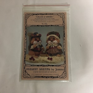 May include: A pattern for making two 12-inch pilgrim squirrel dolls named Caleb and Sarah. The pattern is from Present Dreams by Jeanne, a company that makes original doll and soft art patterns. The pattern is printed on a white background with a brown border and features a picture of the two dolls.