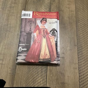 Könnte beinhalten: Ein Renaissance-Kostüm-Schnittmuster mit einer Frau in einem roten und goldenen Kleid mit Maske. Das Schnittmuster trägt den Titel "Renaissance Costume Collection" und enthält den Text "Simplicity Trims" und "Con-so".