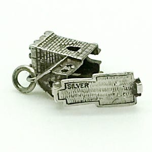 Puede incluir: Encanto de plata de una peque&ntilde;a casa con una fachada de ladrillo detallada y un techo con bisagras que se abre para revelar una inscripci&oacute;n de plata que dice "SILVER".