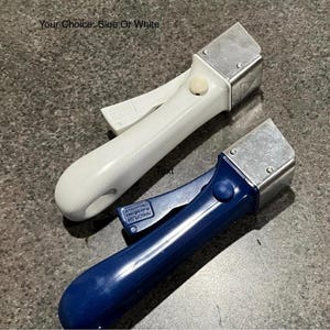 Peut inclure: Deux poignées de batterie de cuisine amovibles, une blanche et une bleue, chacune dotée d'une tête de fixation métallique, d'un levier de déverrouillage et d'un bouton central. Le texte "Your Choice: Blue Or White" est visible au-dessus.