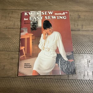 May include: A vintage sewing pattern book titled "KWIK SEW method for EASY SEWING" with a woman in a white outfit on the cover. The book is on a wooden surface. The cover also includes the text "Master Patterns Included".