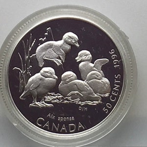 May include: A silver Canadian 50 cent coin from 1996 featuring a design of four ducklings. The coin has the text "50 CENTS 1996" on the right side and "CANADA" on the bottom. The coin also has the text "Aix sponsa" and "DJH" on the bottom.