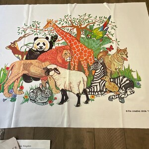 May include: A white fabric wall hanging with a colorful illustration of various animals, including a lion, giraffe, zebra, panda, sheep, rabbit, and a bird. The text "The Creative Circle 1978" is printed in the bottom right corner.