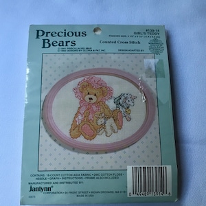 Peut inclure: Un modèle de point de croix compté représentant un ours en peluche rose avec un nœud rose et deux plus petits animaux en peluche. Le modèle est intitulé "Girl's Teddy" et fait partie de la collection "Precious Bears". La taille finie est de 11,4 cm sur 8,9 cm.